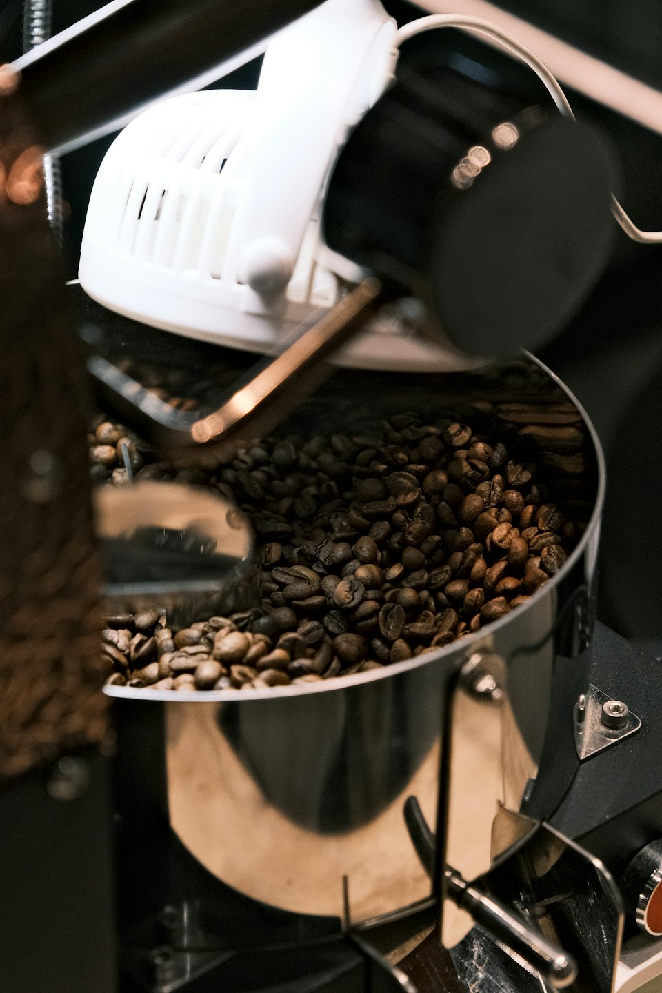 Ristede kaffebønner faller rundt inne i en trommel på en kaffebrenner i rustfritt stål.