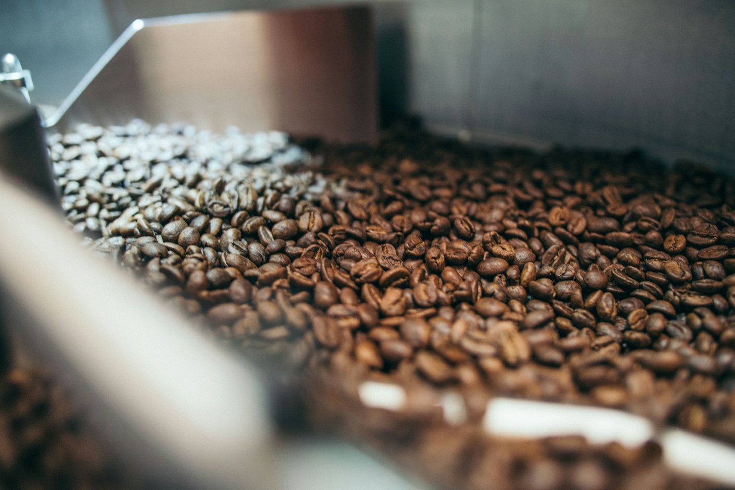 Nybrente kaffebønner som faller i en maskin av metall.